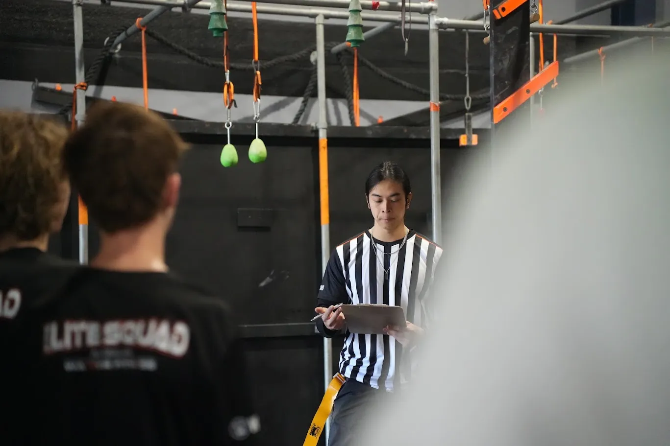 Referee with clipboard judging as Elite Squad athletes look on
