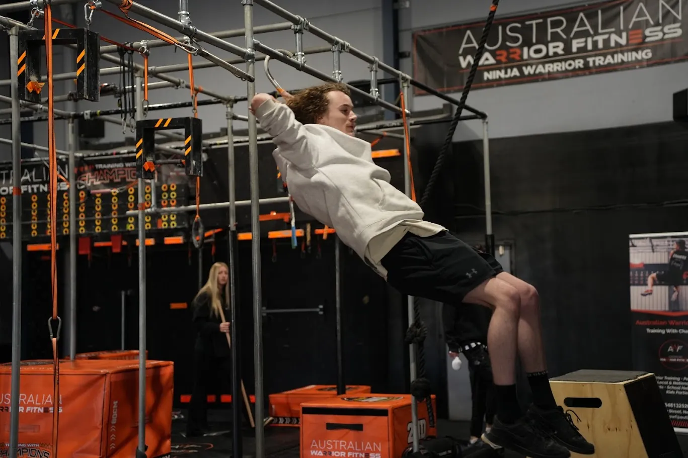 Competitor in a white hoodie swinging between bars on the ninja rig