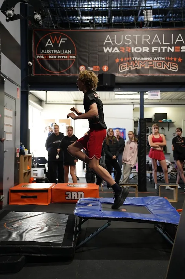 Competitor jumping onto a mini trampoline as officials watch