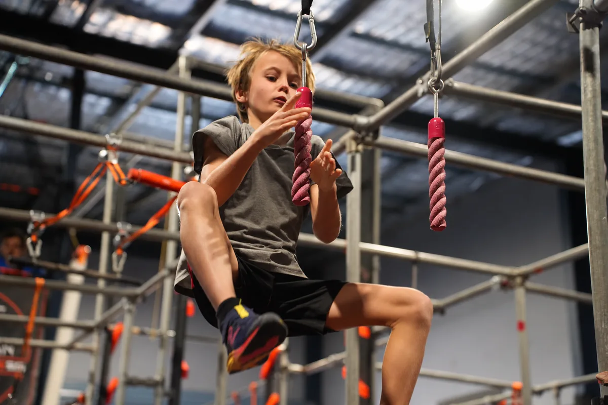 Young ninja in grey reaching for the rope grips on the AWF rig
