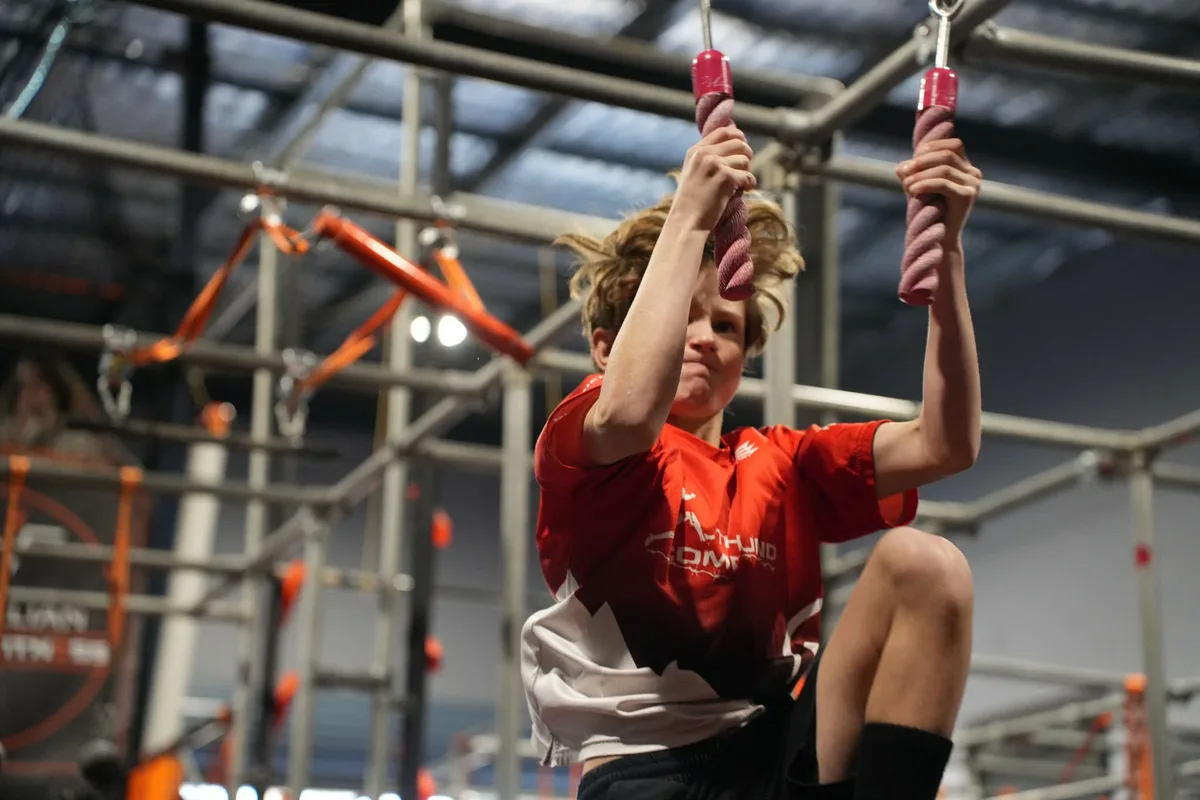 Young competitor in red swinging on the rope grips